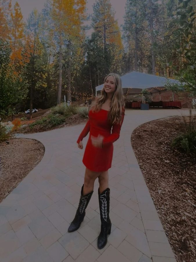 Gwen in a red dress and black boots on a tree lined path