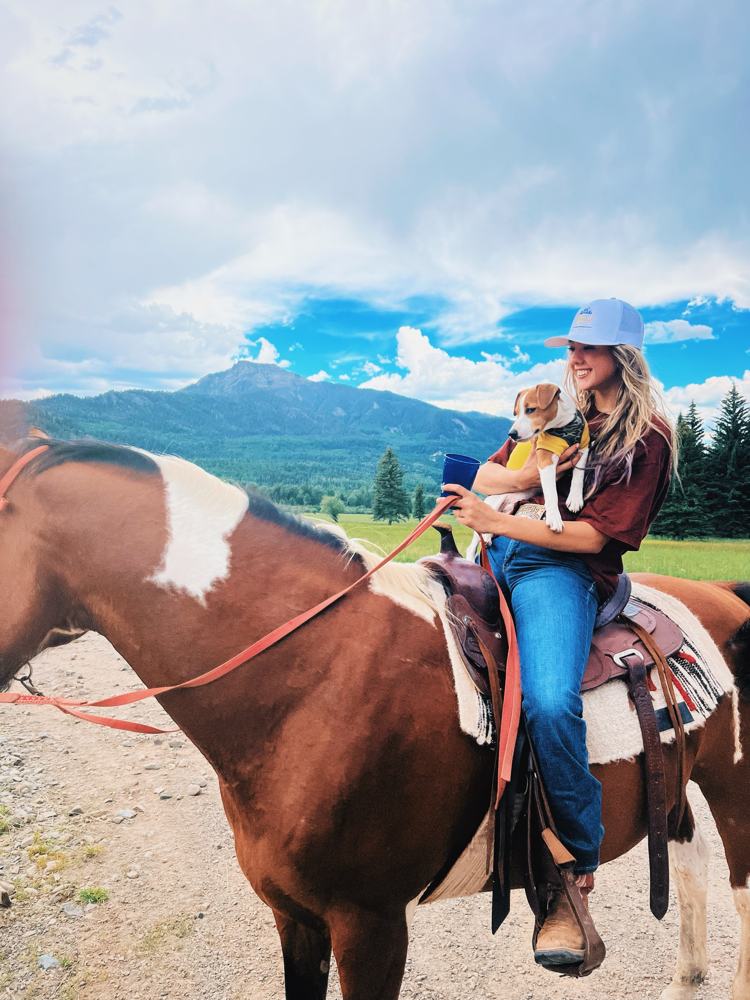 Gwen on a paint horse in the mountains, holding her dog
